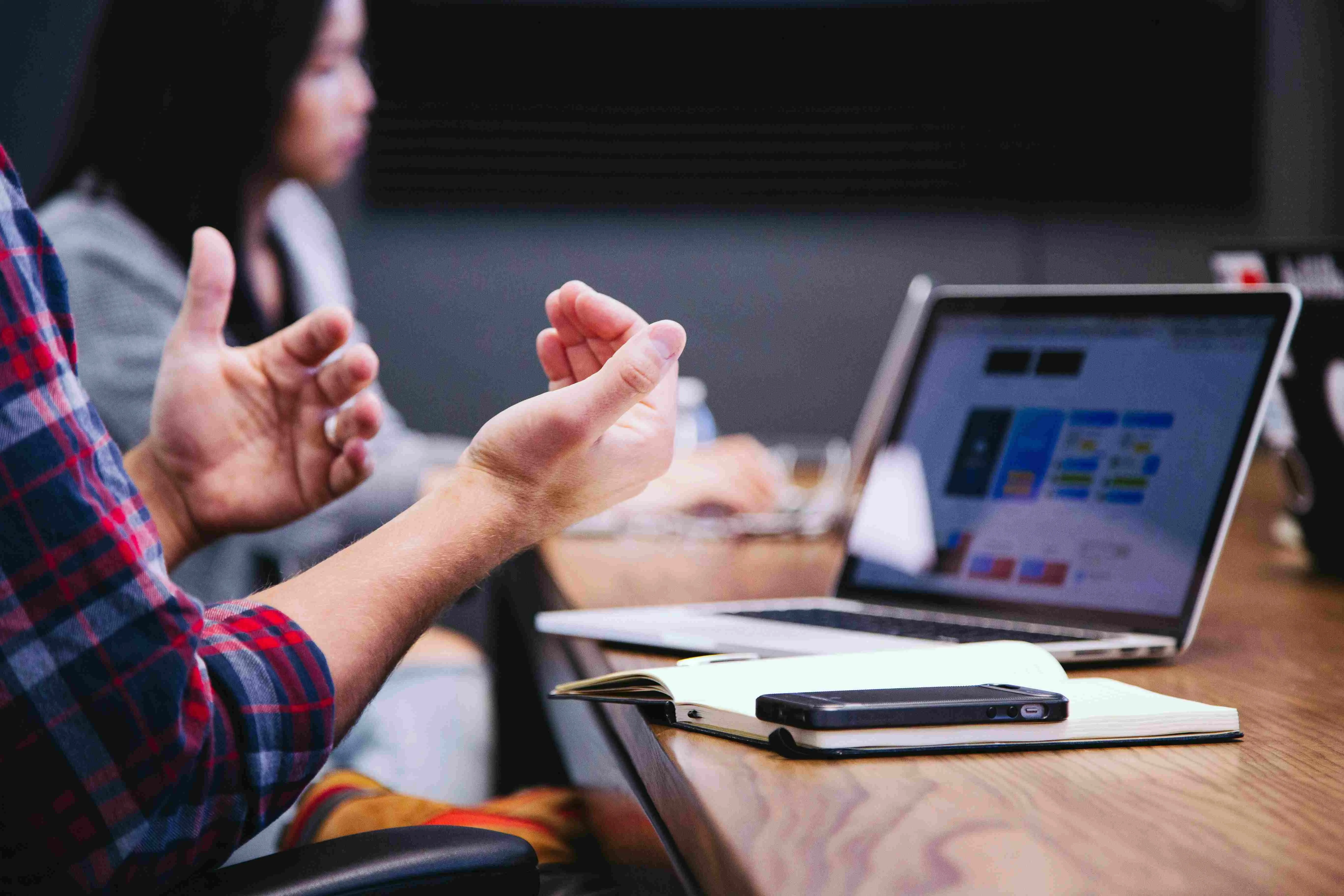 Image of an employee gesturing communicating with his hands sitting in a meeting with his laptop