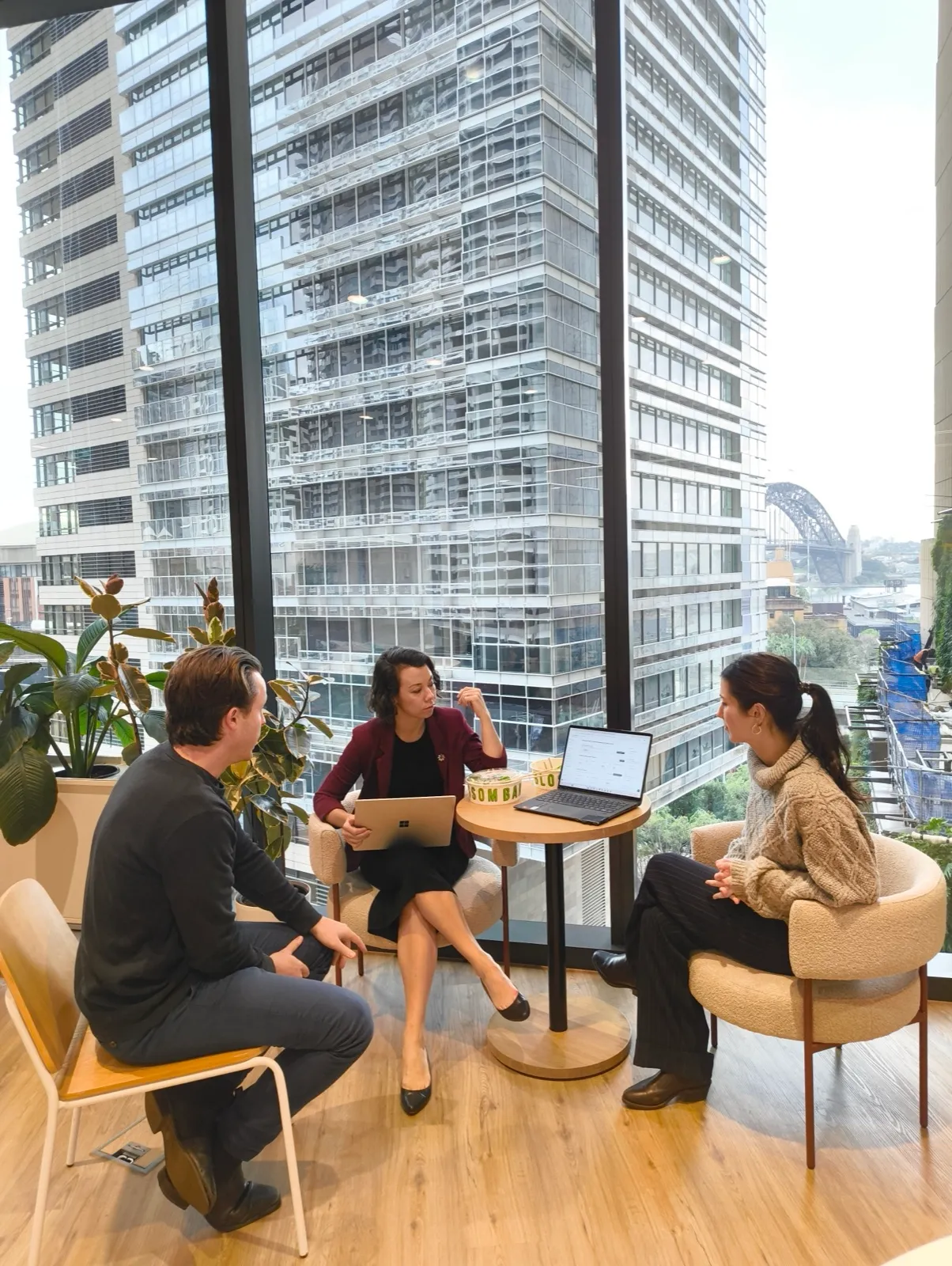 Three team members in a catch-up at the Sydney office, Harbour Bridge in the window